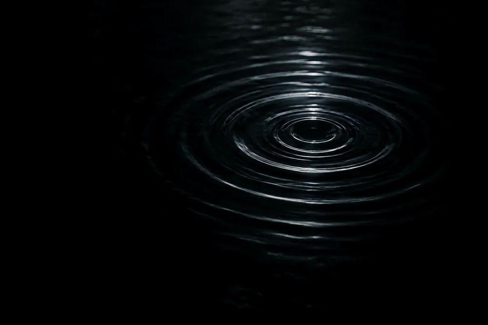Una sola onda que se expande sobre agua oscura y quieta